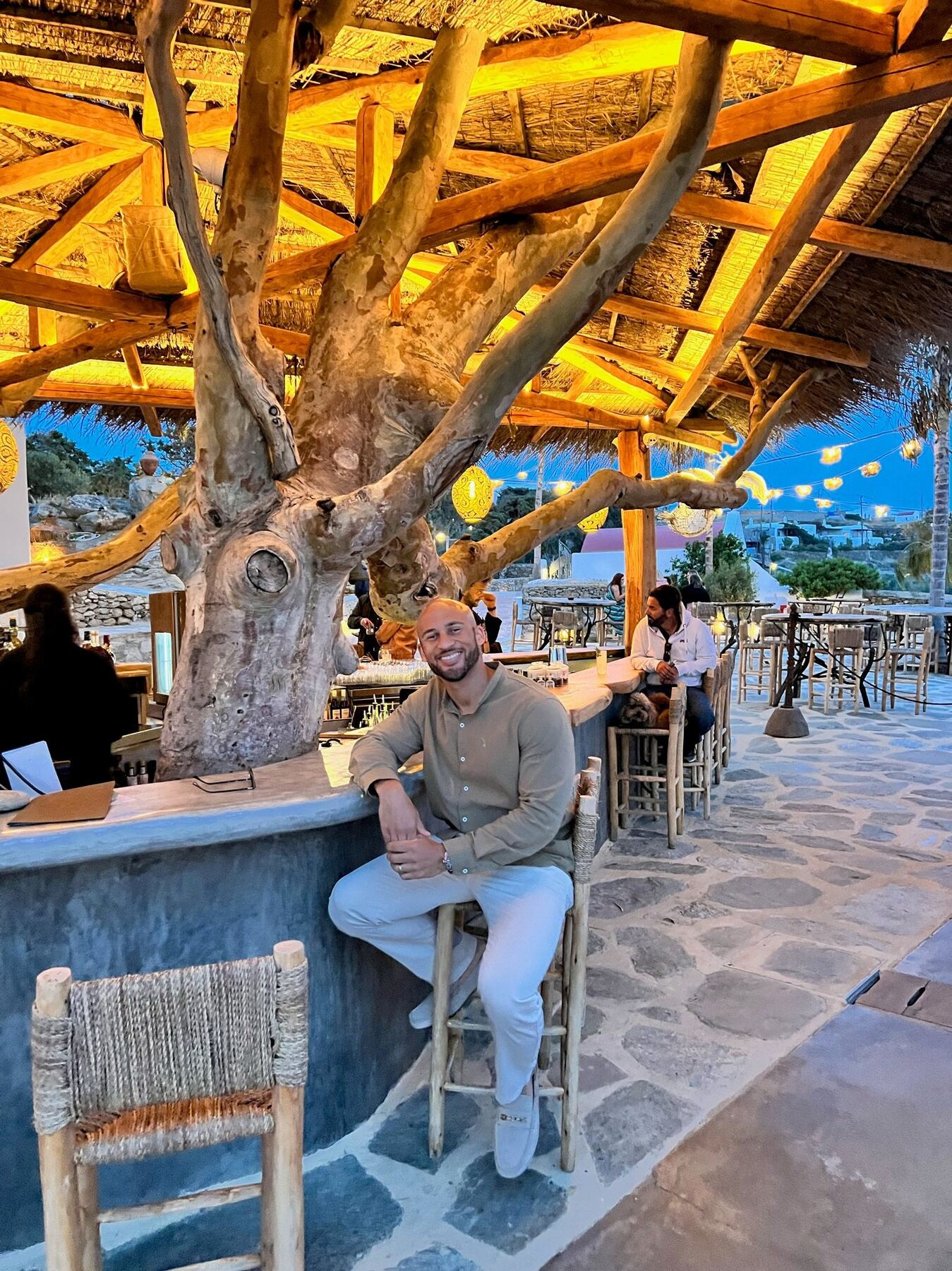 A traveler seated beneath a sculptural tree at an open-air Mykonos terrace